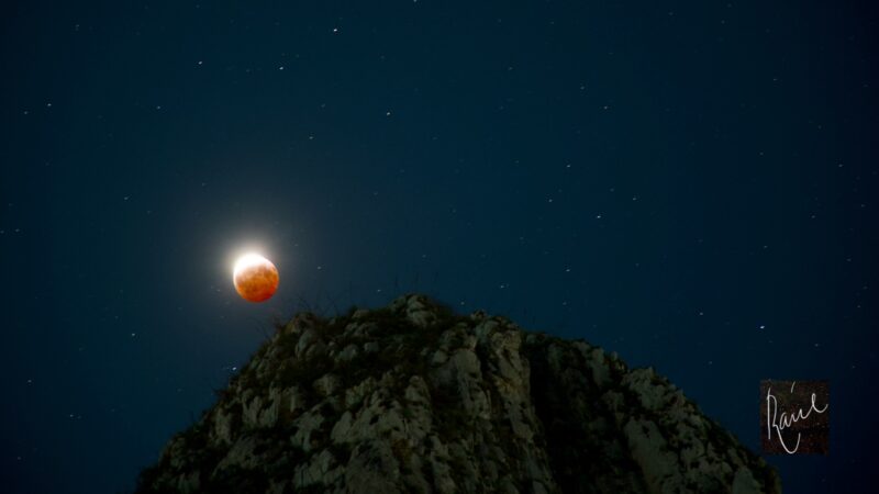 Red lunar eclipse over a rocky hillside.