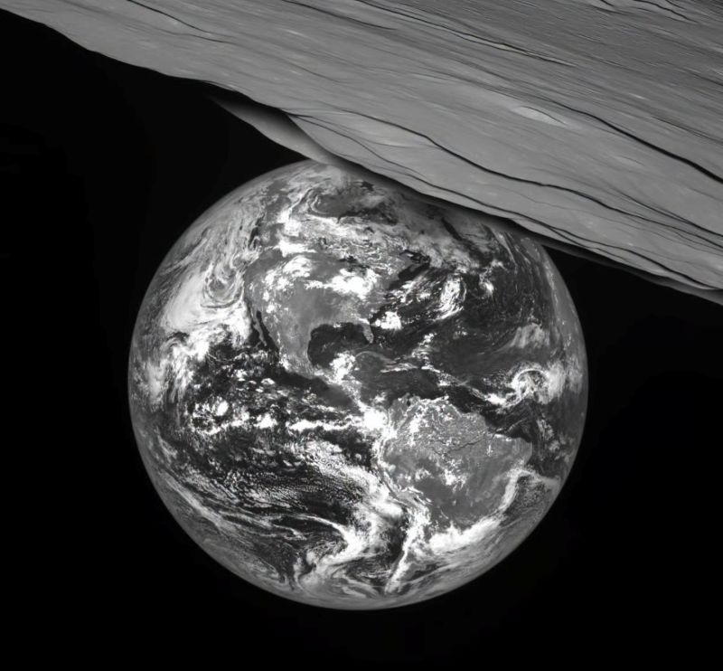 Solar eclipse: Black and white closeup of part of moon at top right with Earth partly behind its horizon, and a dark area on Earth.