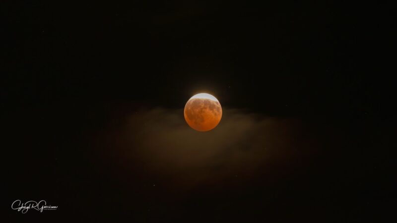 Orange, eclipsed moon, with thin clouds below.