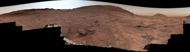 Wide view of brownish terrain with a couple of hills under a dusty sky.