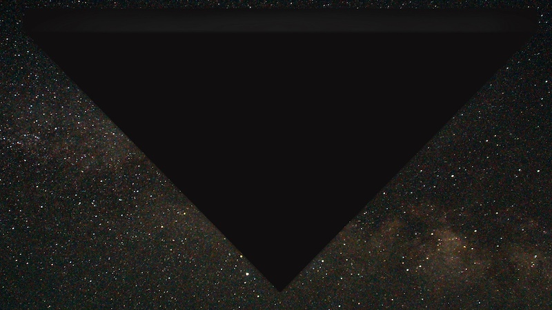Large solid black triangular object blotting out stars in the night sky.
