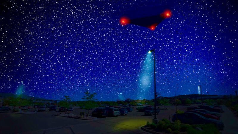 Pentagon UAP files: Black triangular-shaped object in a dark blue light sky with many stars in the background. A red light is at each corner of the triangle.