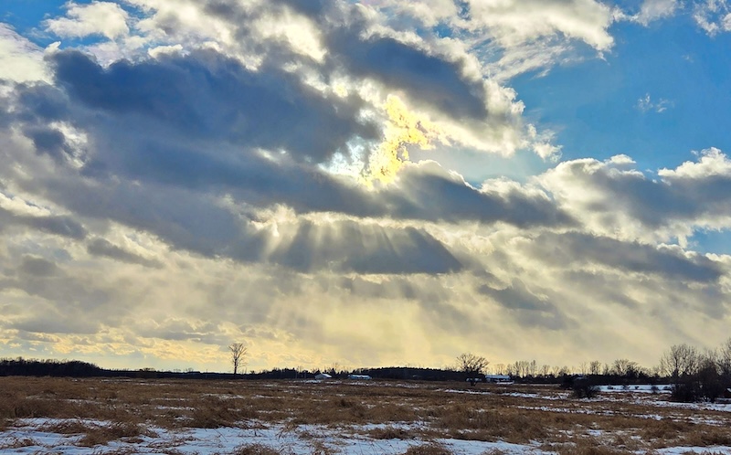 Crepuscular rays coming out of several cloud layers over prairie land.