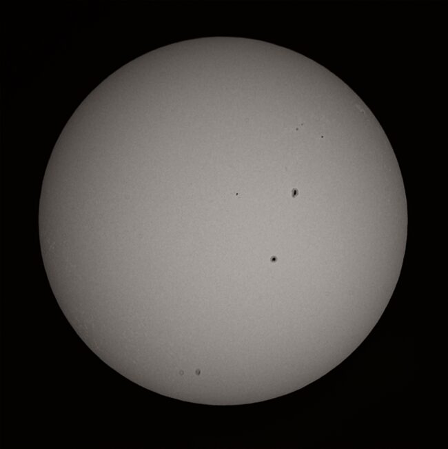 The sun, seen as a large gray sphere with small dark spots.