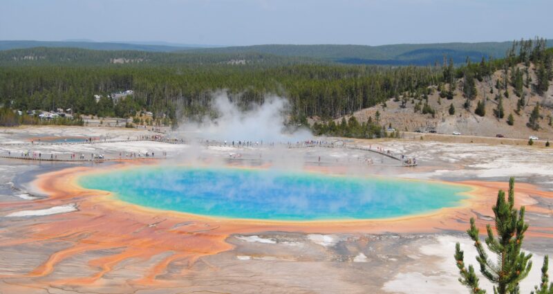 A bright blue pool with steam and ringed in rainbow hues plus people on boardwalks around it.