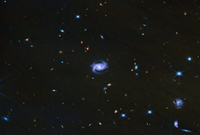 A bluish, distinctly spiral galaxy at center with very many smaller ones scattered around.