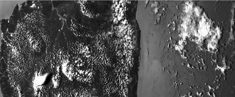 Black and white view from space at dark, rugged land on left plus a river and clouds, sea on right.