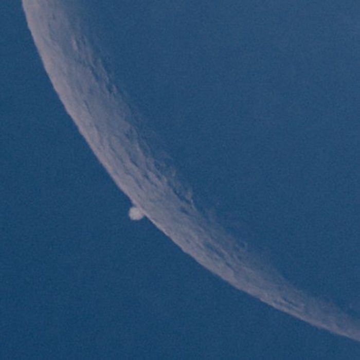 Part of the crescent moon with a bright dot at the very edge of the lit part.