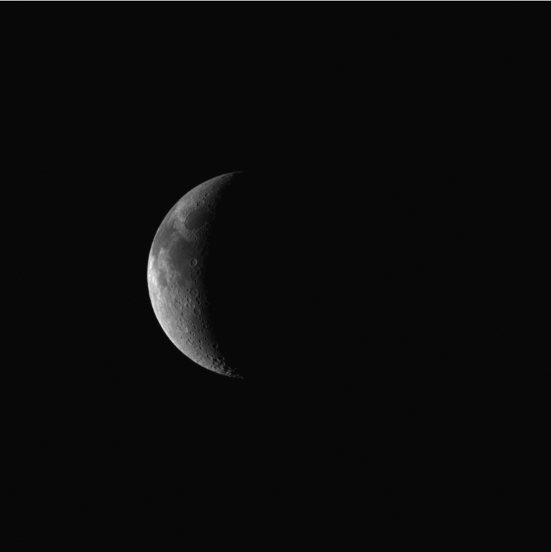 The dim crescent moon in black space with the left side lit.