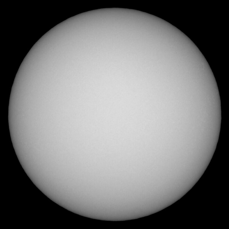 The sun, seen as a large white sphere with small dark spots.