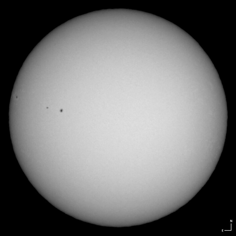 The sun, seen as a large white sphere with small dark spots.