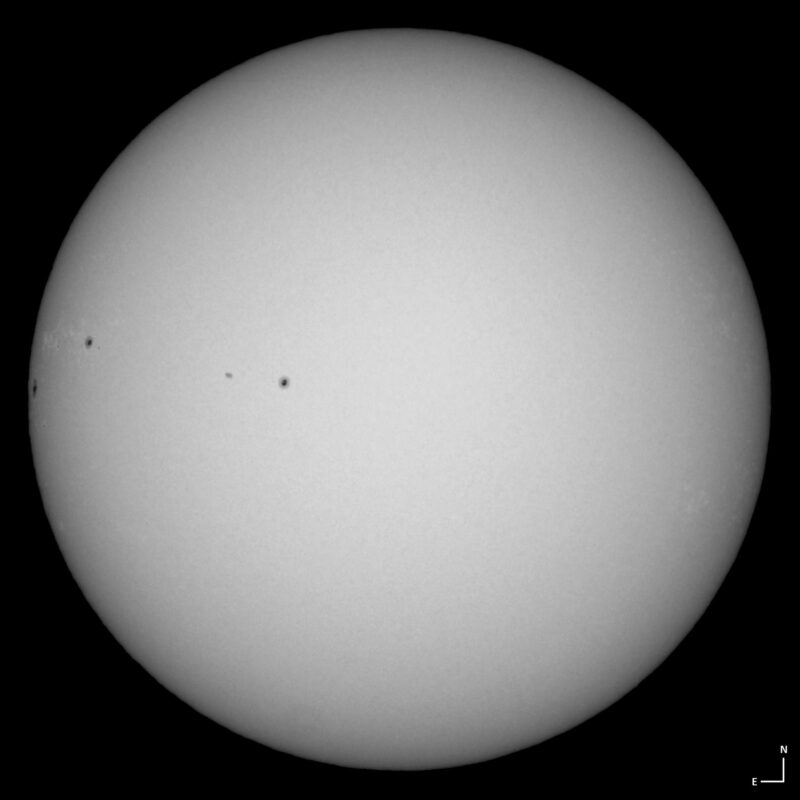 The sun, seen as a large white sphere with small dark spots.