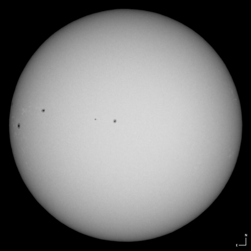 The sun, seen as a large white sphere with small dark spots.