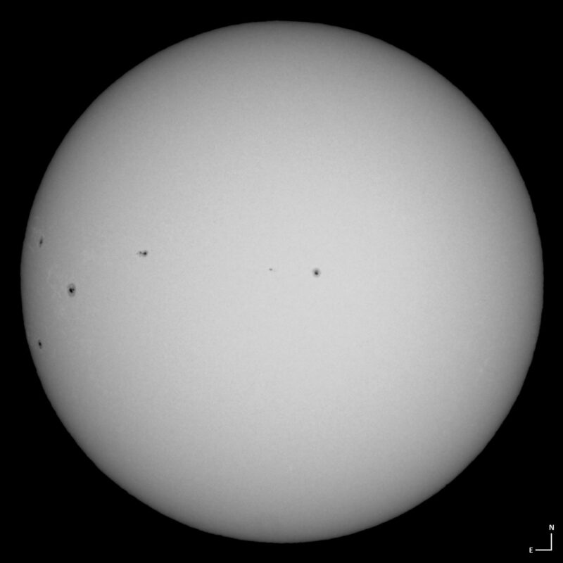 The sun, seen as a large white sphere with small dark spots.