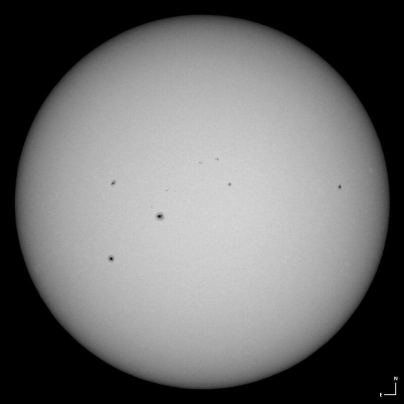 The sun, seen as a large white sphere with small dark spots.