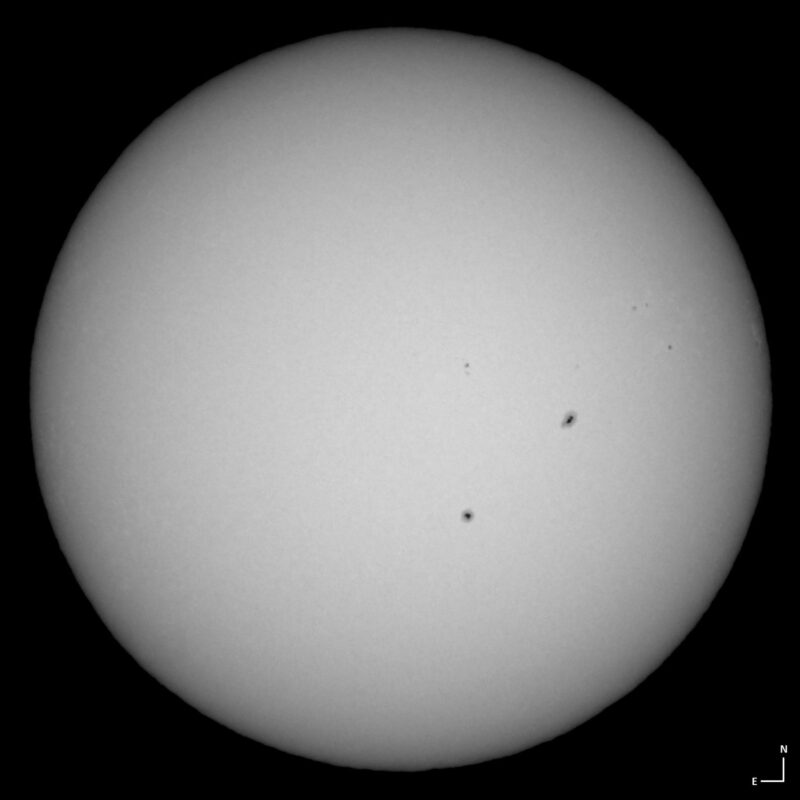 The sun, seen as a large white sphere with small dark spots.