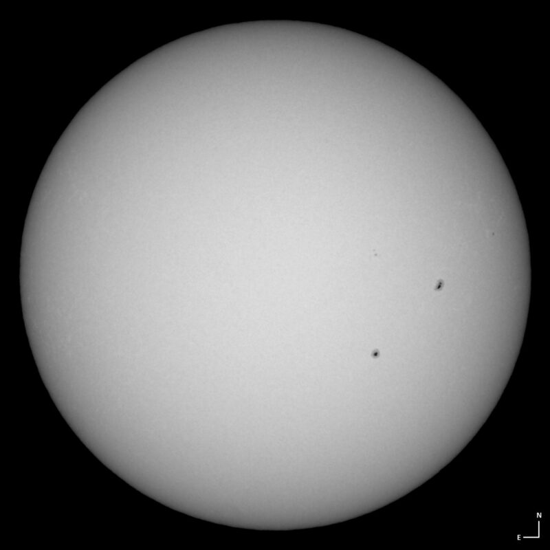 The sun, seen as a large white sphere with small dark spots.