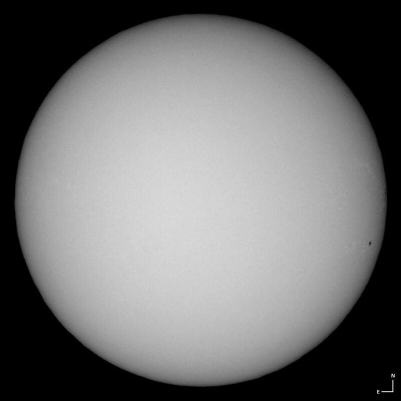 The sun, seen as a large white sphere with small dark spots.