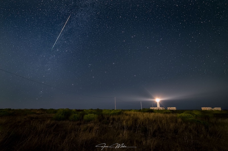Starry sky with a bright Perseid by Cassiopeia. There's a lighthouse to the right.