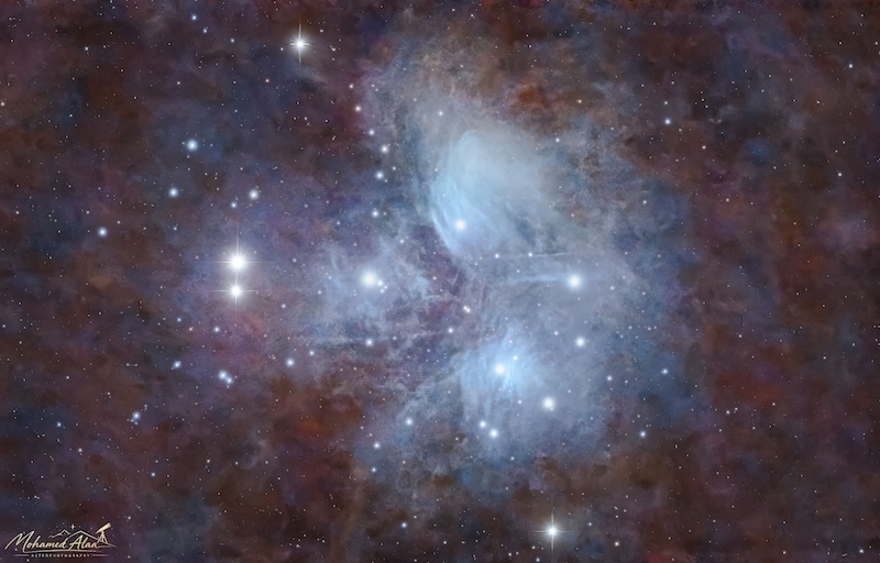 The star cluster Pleiades showing lots of bluish nebulae around the stars and other nebulae nearby.