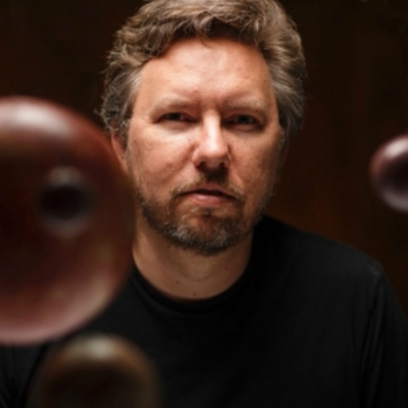Man with brown hair and beard looking at the camera. 3 out of focus spheres are around him.