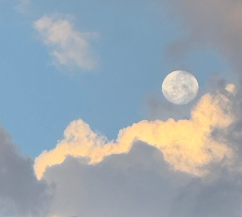 A white, big sphere in a blue sky, with many clouds below.