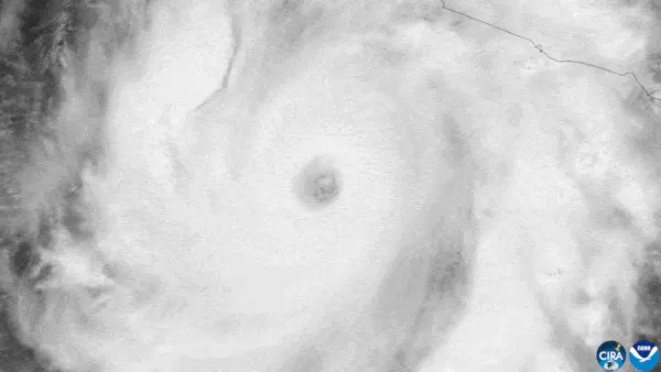 Black and white satellite view down at a large white swirling hurricane with a clearing eye
