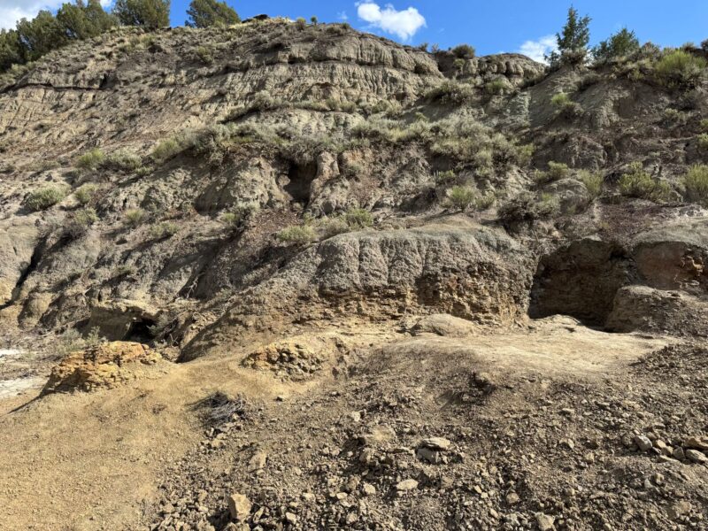 View of rocks with blue sky above. The lighter brown earth has 4 raised protrusions.