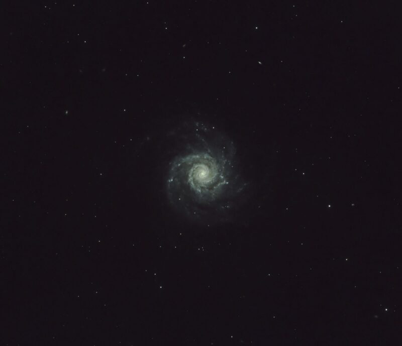 Whitish spiral galaxy seen head-on, with dark lanes and sparse foreground stars.