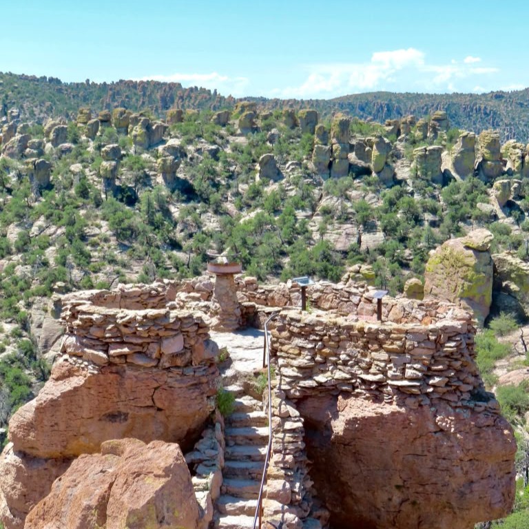 Rocky spires in the background with a viewing platform in front ringed with a rock wall with stairs leading to it.