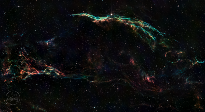 A large, multicolor arc of nebulosity, with numerous stars immersed within and in the surroundings.
