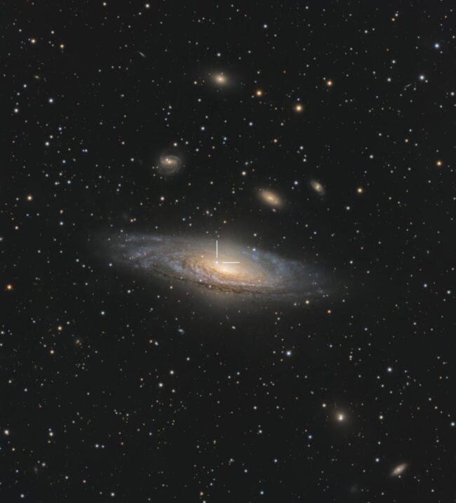 Large, yellowish galaxy, a spiral seen almost edge-on, with white tick marks and numerous foreground stars.