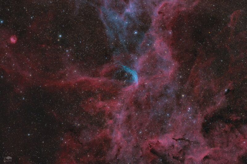 A huge, complex red nebula with small blue swirls and a background of thousands of faint stars.