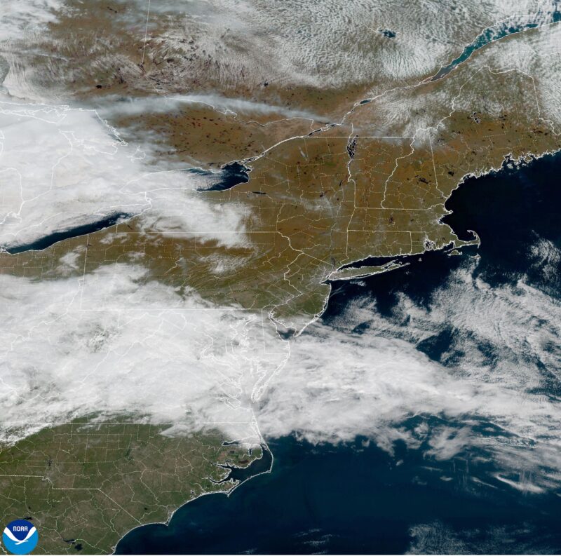 Satellite view of northeast with orange terrain at top and a cloud swath with green terrain in the states below.