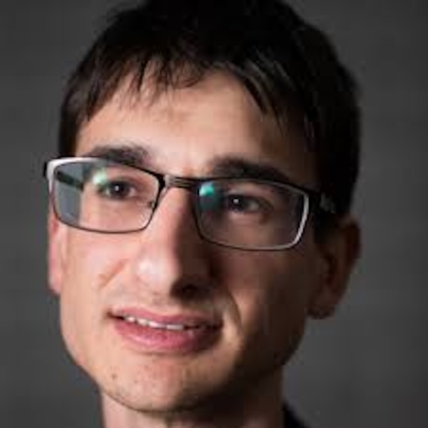 Smiling man with rectangular eyeglasses and short hair.