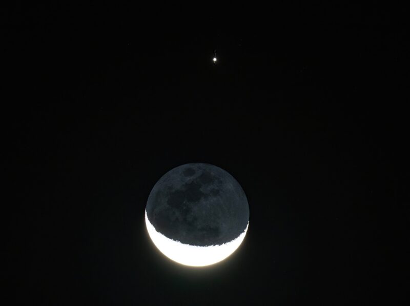 Crescent moon lit at bottom with a bright disk above and dots for moons.