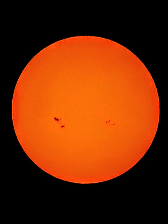 The sun, seen as a large orange sphere with dark spots.