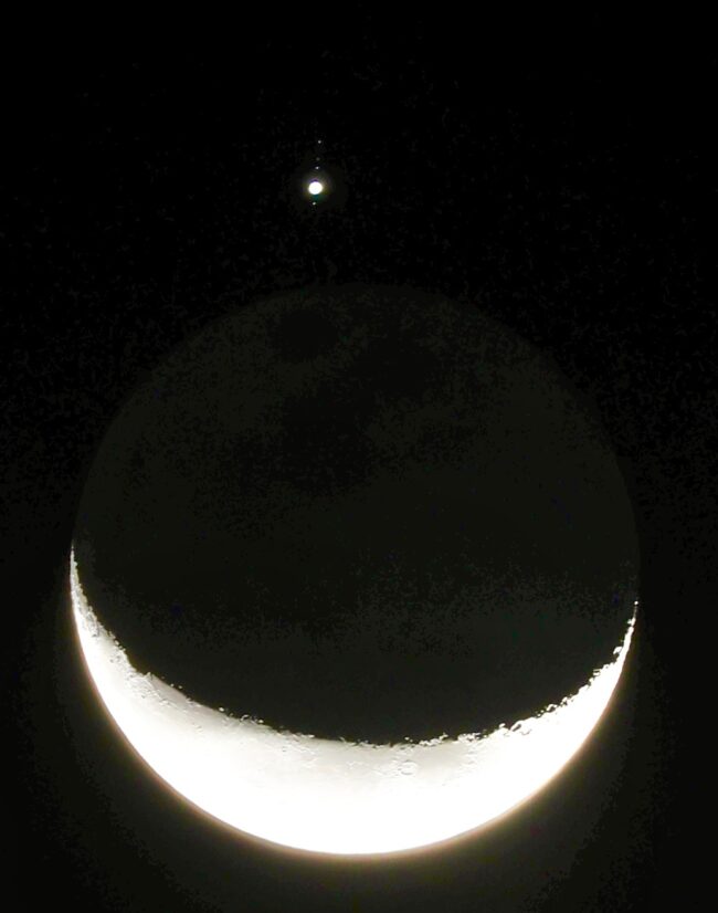 A bright crescent moon with Jupiter above it, with tiny dots aligned in a line.