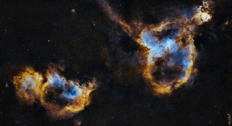 Two large, complex, yellowish mass of gas with blue highlights and numerous foreground stars.