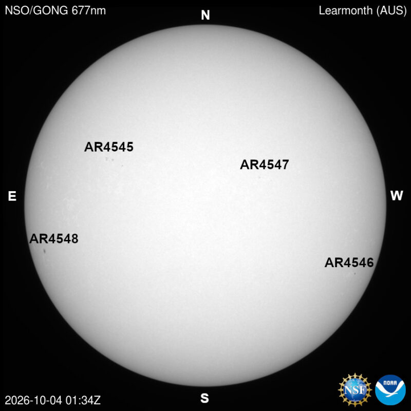 The sun in visible light, a pale disk with a few small dark sunspots, each labeled with its active region number.