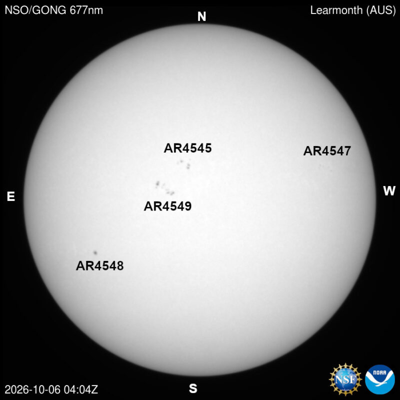 The sun in visible light, a pale disk with a few small dark sunspots, each labeled with its active region number.
