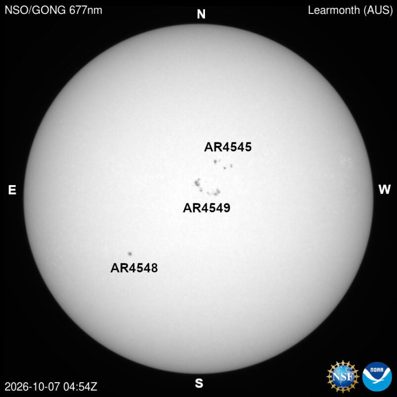The sun in visible light, a pale disk with a few small dark sunspots, each labeled with its active region number.