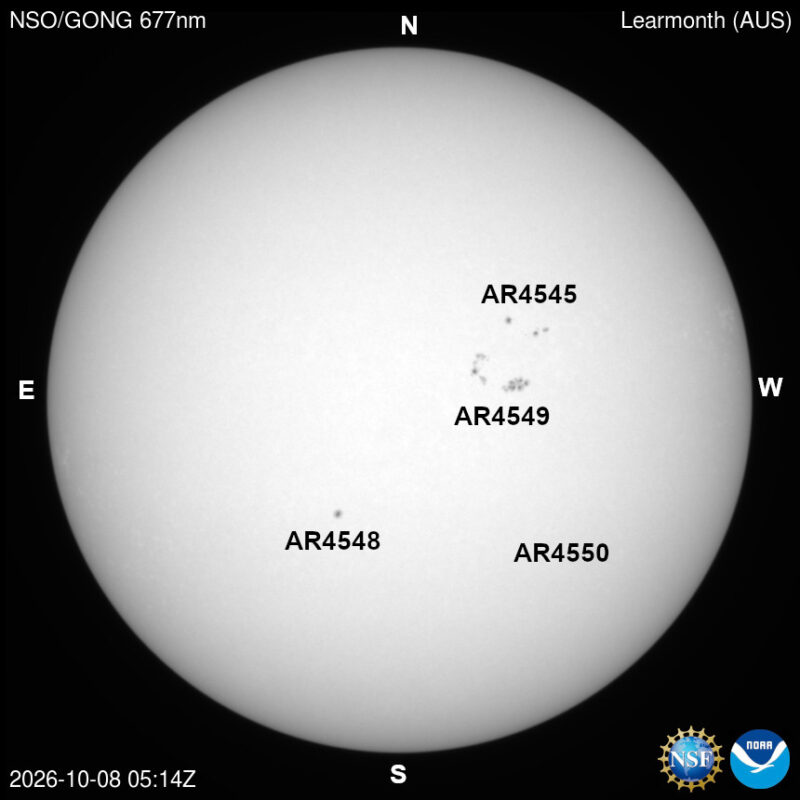 The sun in visible light, a pale disk with a few small dark sunspots, each labeled with its active region number.