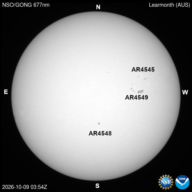 The sun in visible light, a pale disk with a few small dark sunspots, each labeled with its active region number.