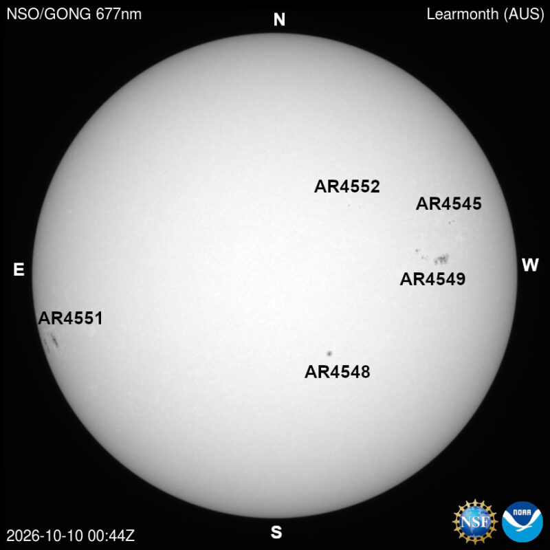 The sun in visible light, a pale disk with a few small dark sunspots, each labeled with its active region number.