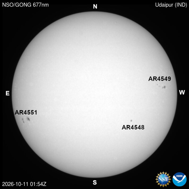 The sun in visible light, a pale disk with a few small dark sunspots, each labeled with its active region number.