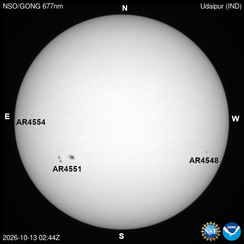 The sun in visible light, a pale disk with a few small dark sunspots, each labeled with its active region number.