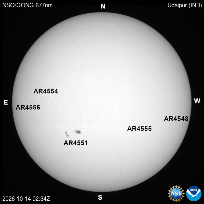 The sun in visible light, a pale disk with a few small dark sunspots, each labeled with its active region number.