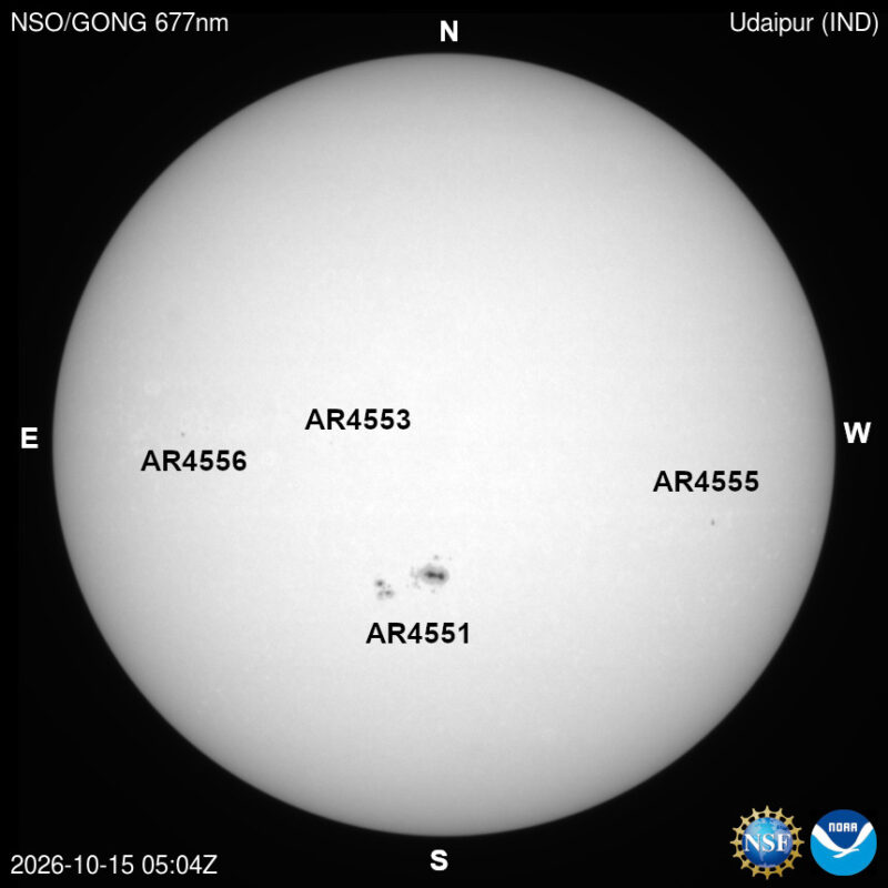 The sun in visible light, a pale disk with a few small dark sunspots, each labeled with its active region number.