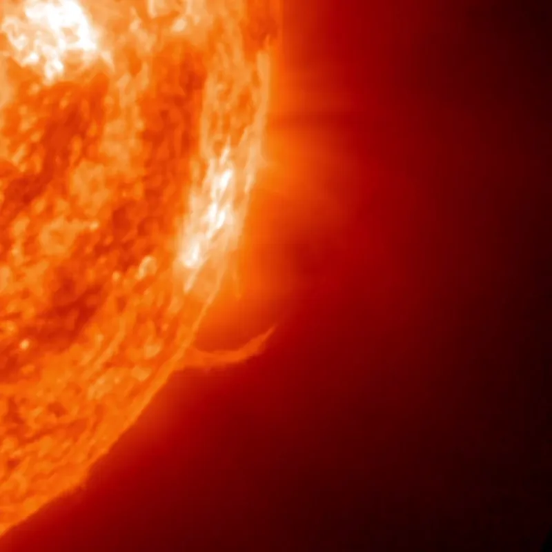 The sun's southwest edge glowing orange-red, with jets and prominences rising from a departing active region.